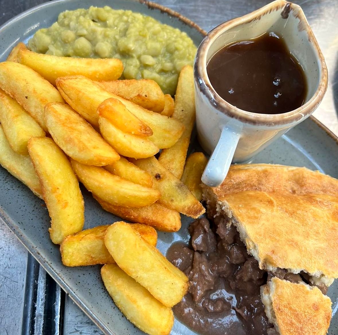 A pie with chips, mushy peas and a jug of gravy